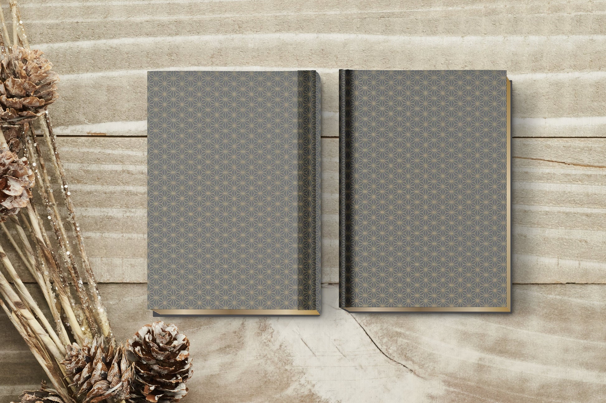 Two gray patterned books made with chiyogami paper in a bookbinding project on a wooden surface with dried plants.