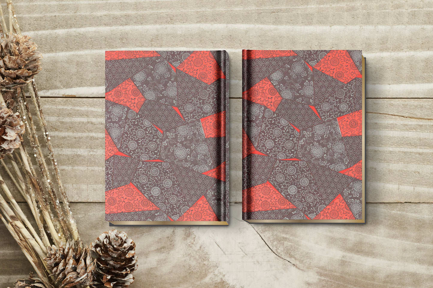Two notebooks with red and gray geometric pattern wrapped with chiyogami paper on a wooden surface with pine cones.
