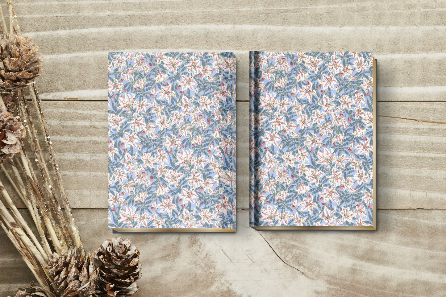 Two floral-patterned notebooks made with chiyogami paper for a bookbinding project on a wooden surface with dried plants.