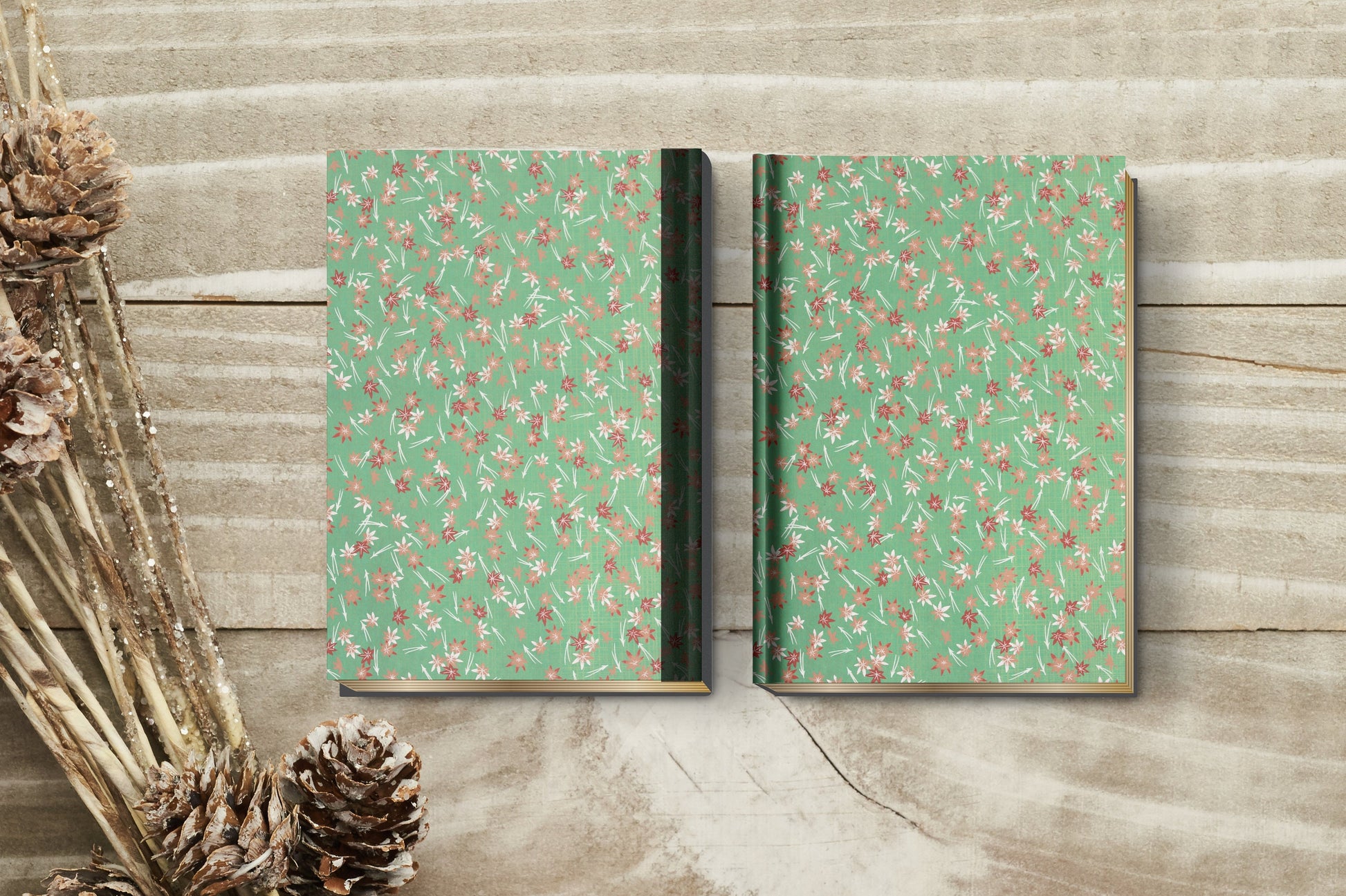 Two green notebooks made with chiyogami paper in a bookbinding project with floral patterns on a wooden surface.