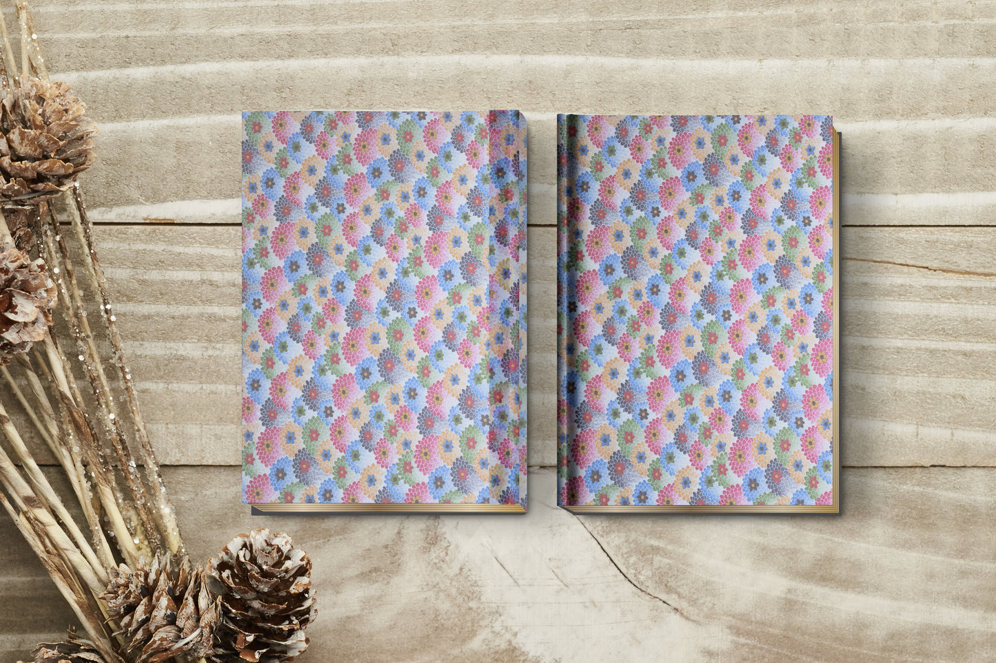 Two floral-patterned notebooks made with chiyogami paper in a bookbinding project on a wooden surface with decorative elements.