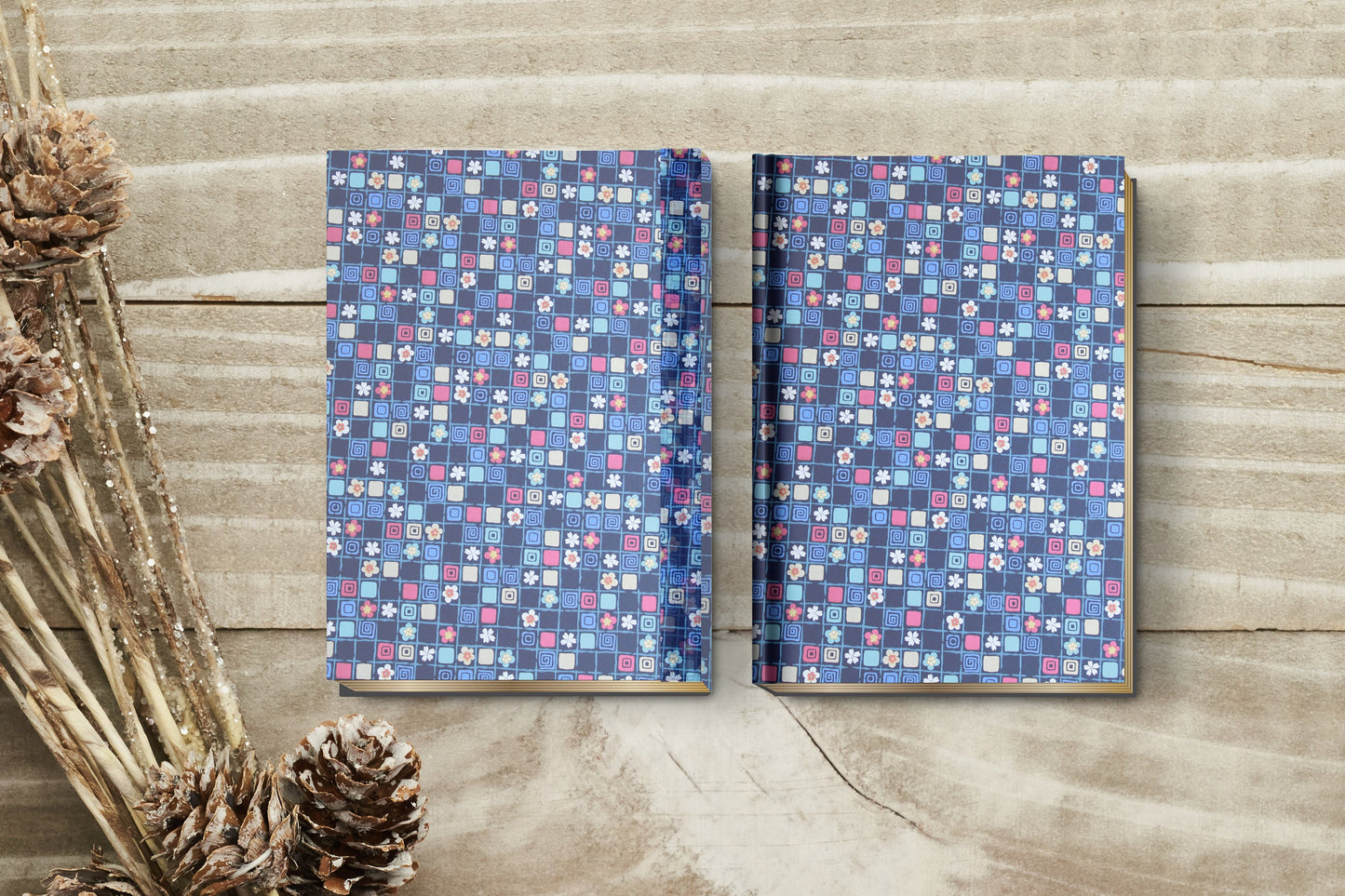 Two notebooks with a blue floral pattern made with chiyogami paper in a bookbinding project on a wooden surface with pine cones.