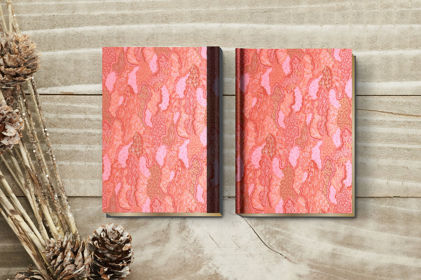 Two notebooks with red and pink pattern wrapped with chiyogami paper on a wooden surface with pine cones.
