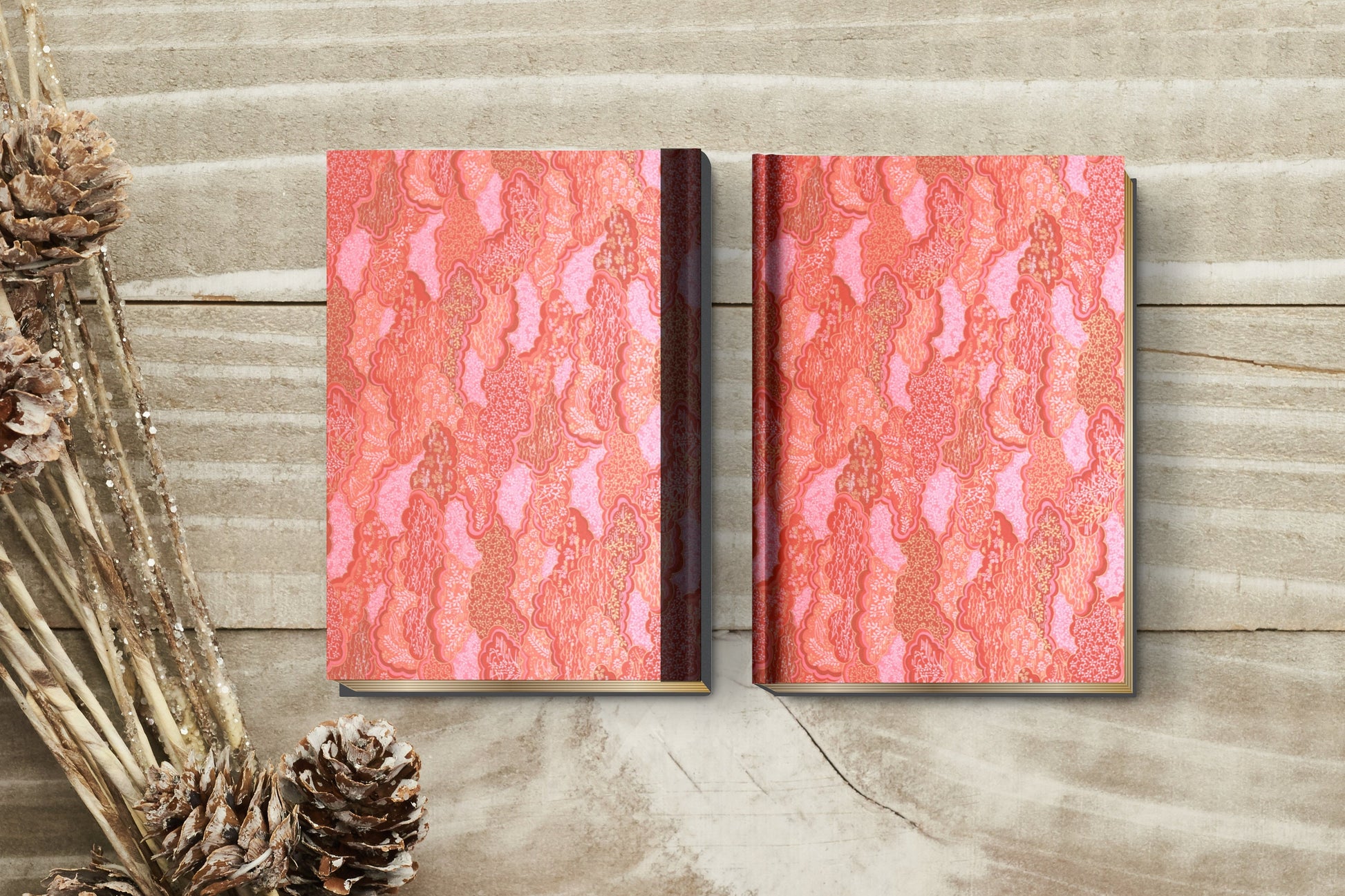Two notebooks with red and pink pattern wrapped with chiyogami paper on a wooden surface with pine cones.