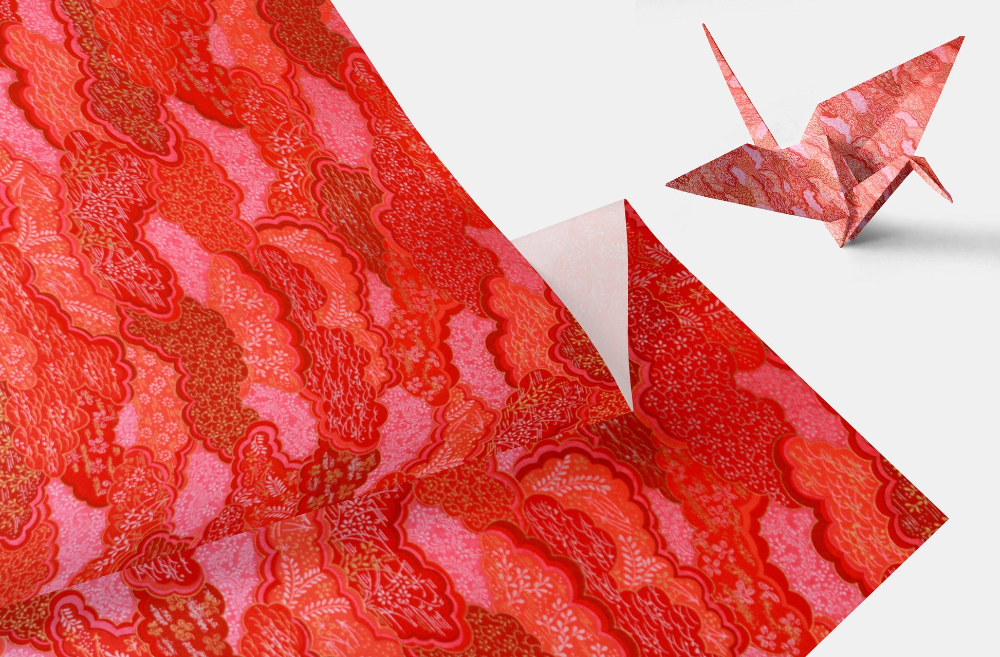 Pink and red patterned chiyogami paper with an origami crane on a white background.