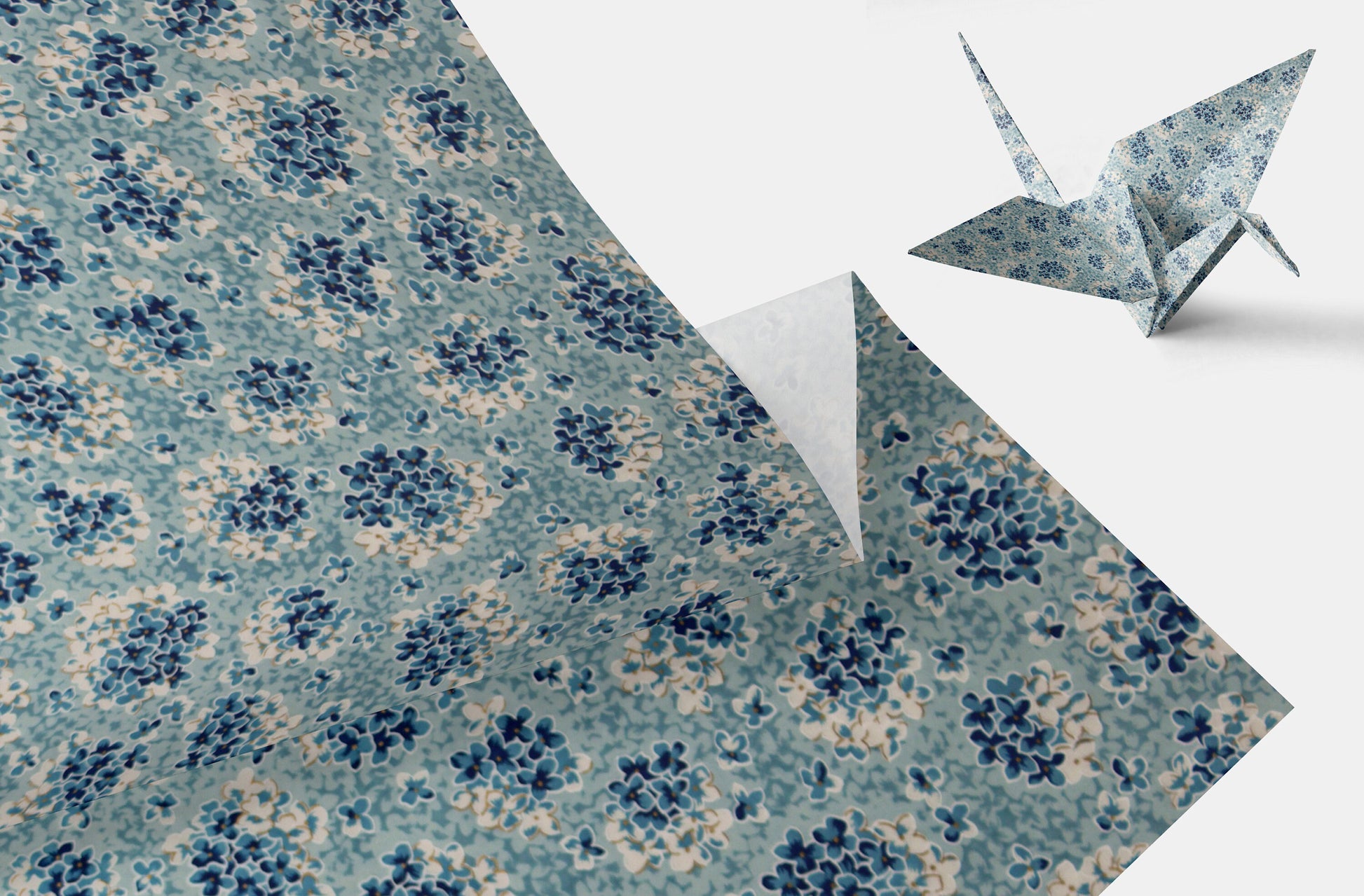 Floral-patterned chiyogami paper with a folded corner and an origami crane on a white background