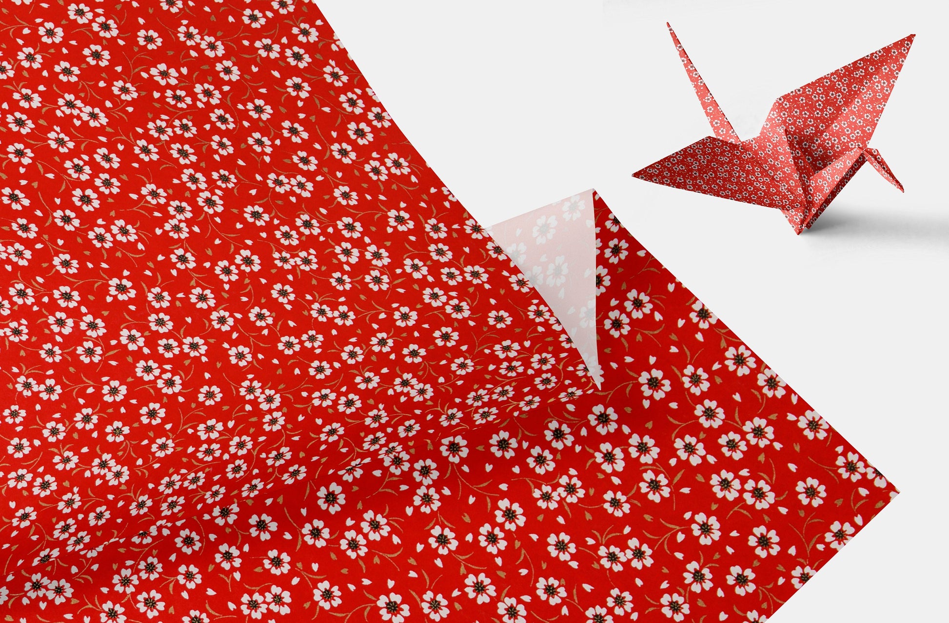 Red floral-patterned paper with a folded corner and an origami crane on a white background