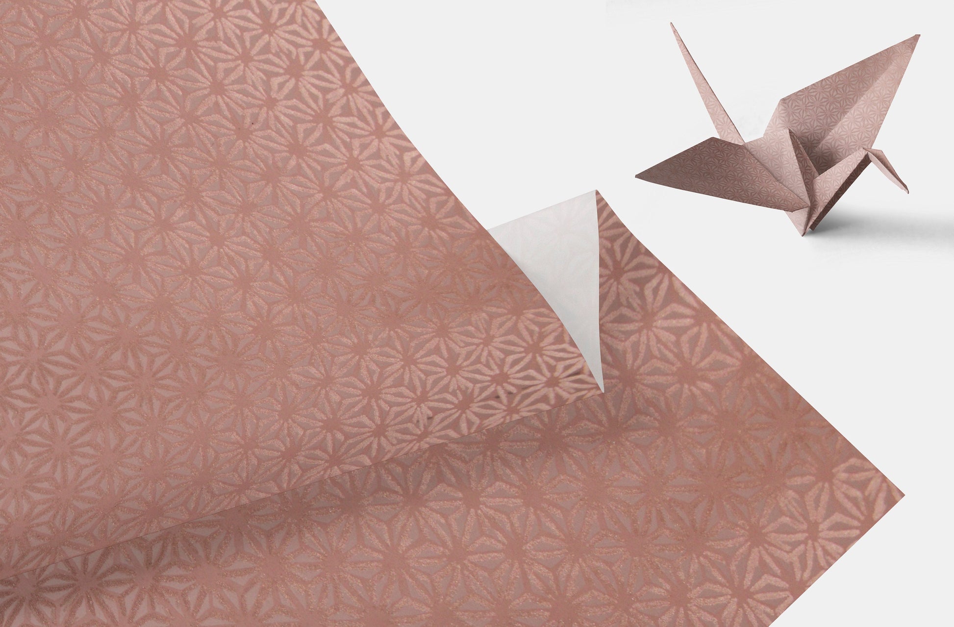 Patterned pink chiyogami paper with a folded origami crane on a white background