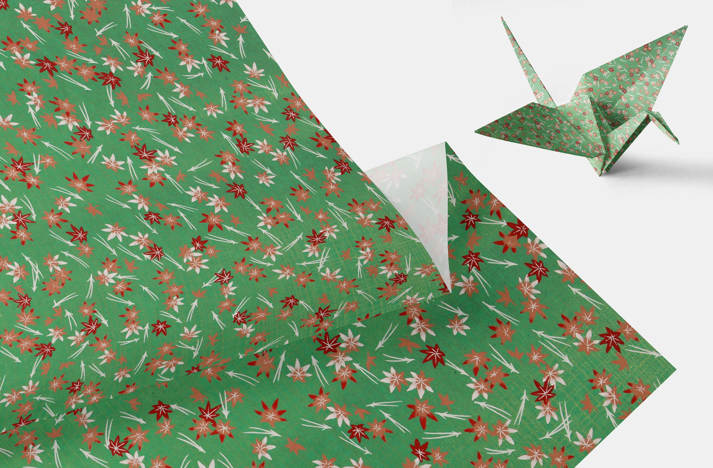 Green floral-patterned chiyogami paper with a folded corner and a green origami crane on a white background