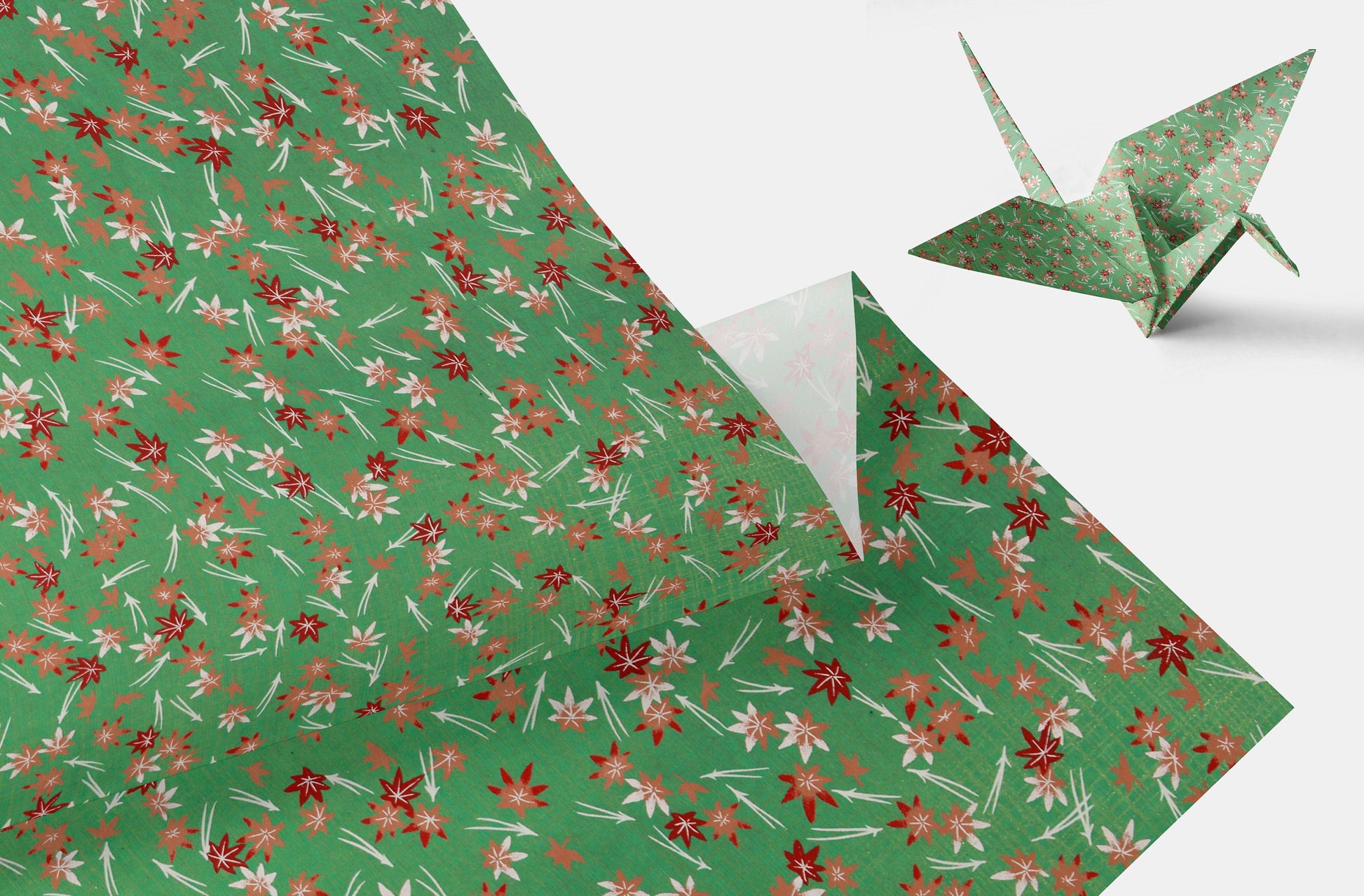 Green floral-patterned chiyogami paper with a folded corner and a green origami crane on a white background