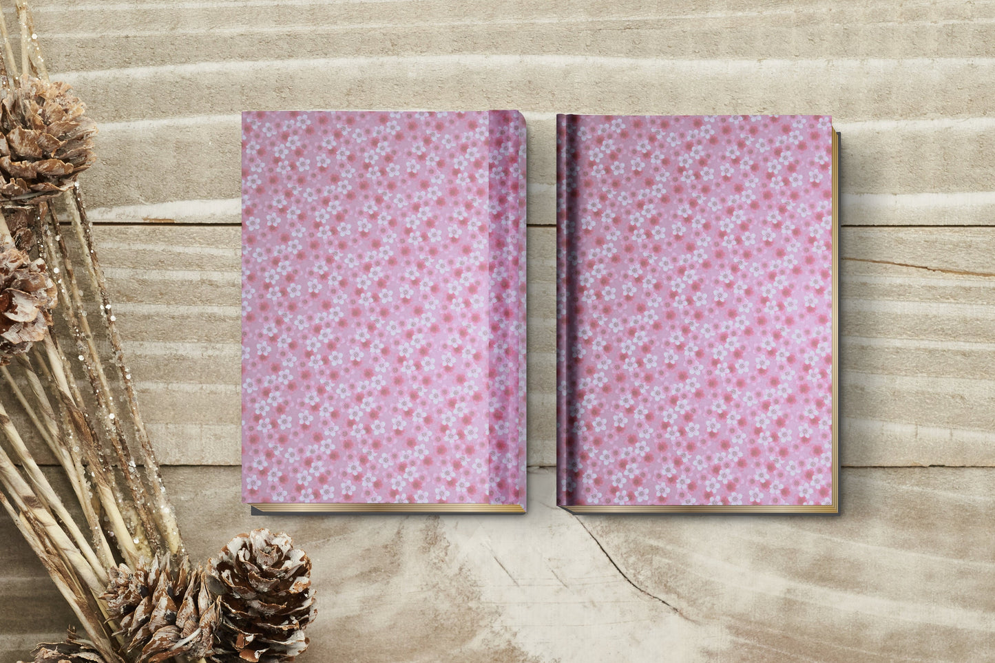 Two pink floral-patterned notebooks made with chiyogami paper in a bookbinding project on a wooden surface with dried plants.