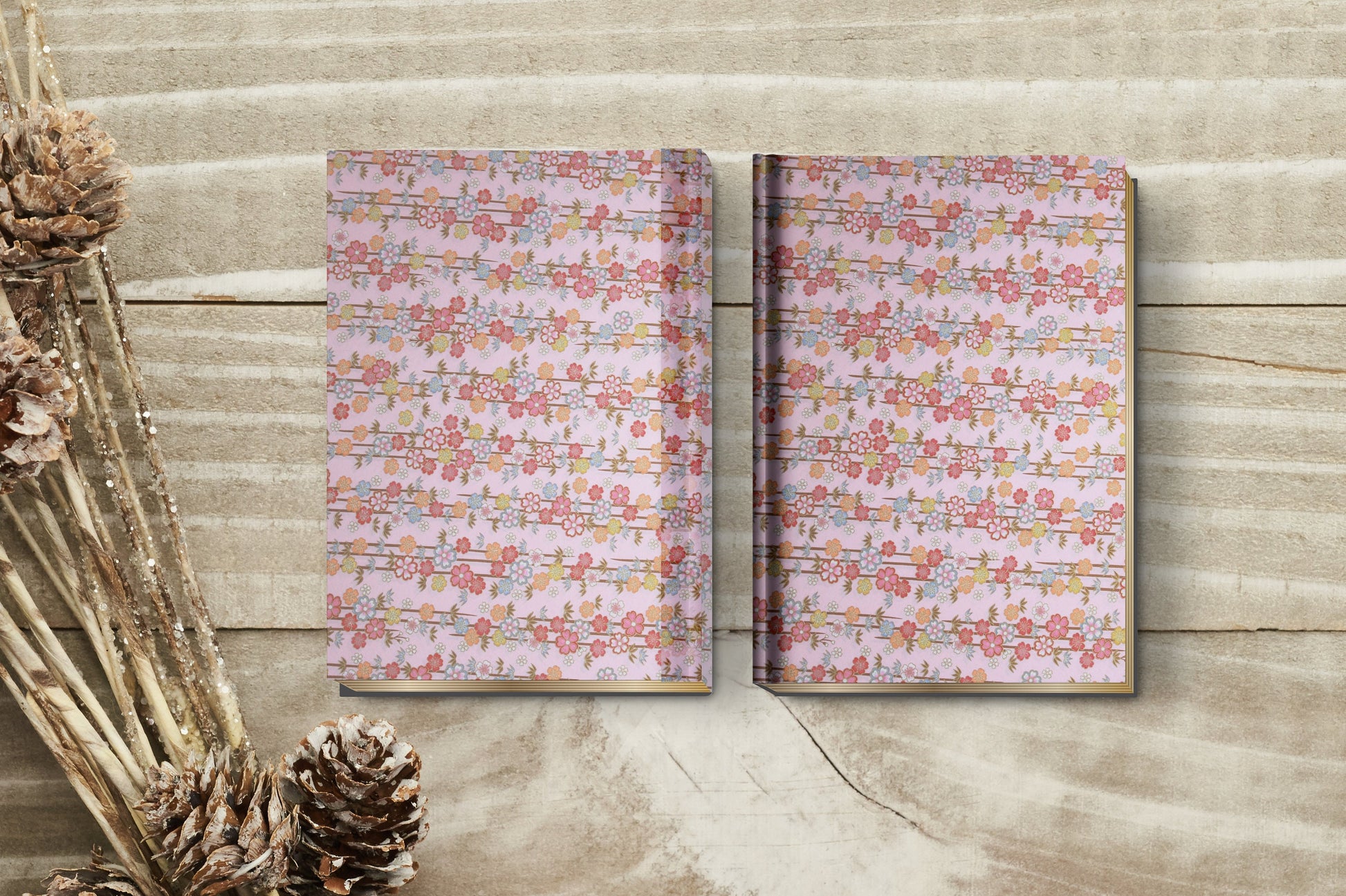 Two floral-patterned notebooks made with chiyogami paper in a bookbinding project on a wooden surface with dried plants.