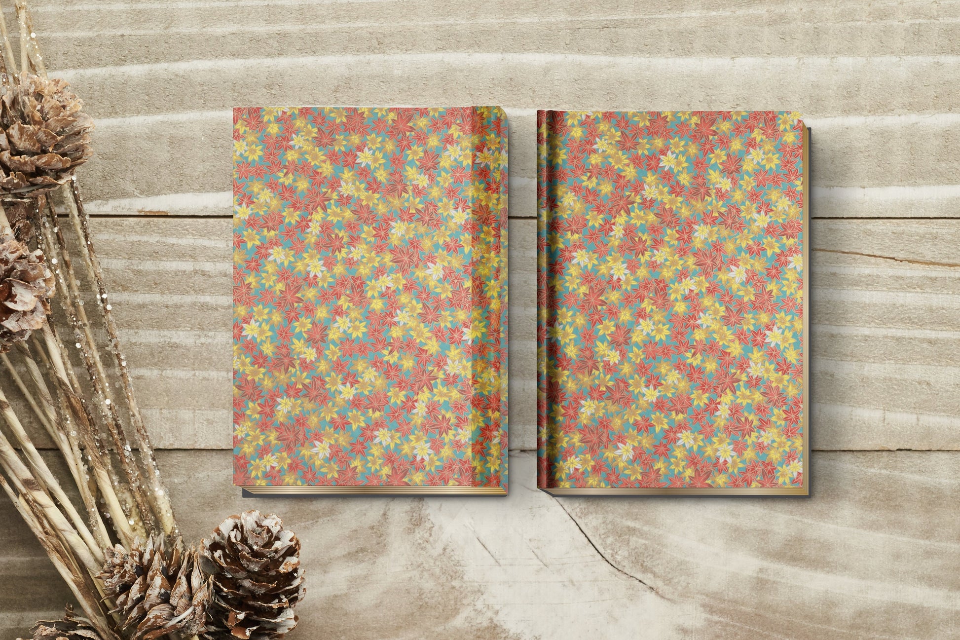 Two floral-patterned notebooks on a wooden surface with pine cones.