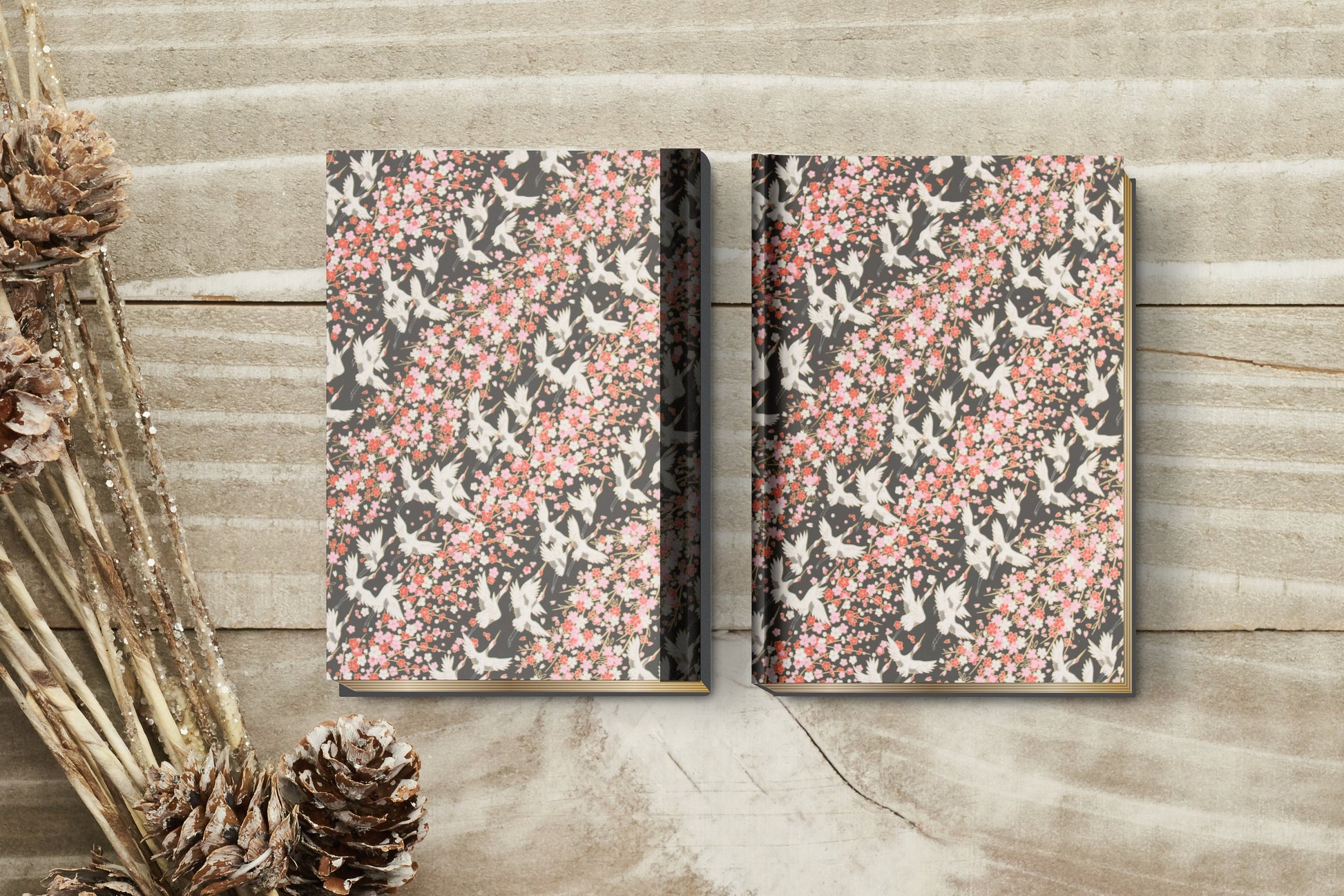 Two floral-patterned books on a wooden surface with dried plants.