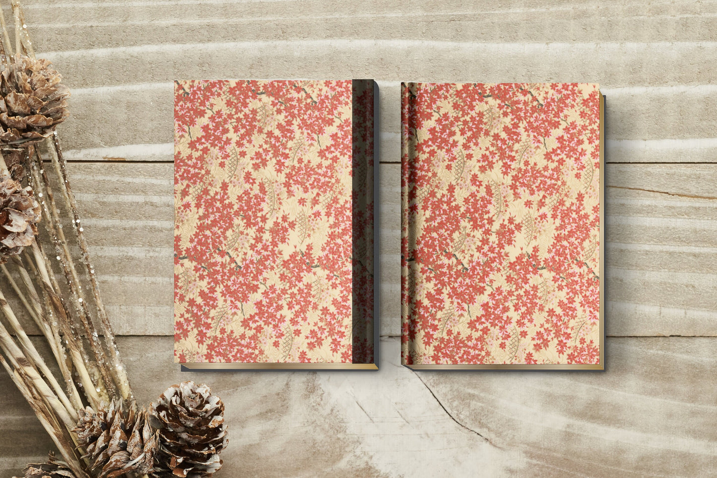 Two floral-patterned books on a wooden surface with pine cones and branches.