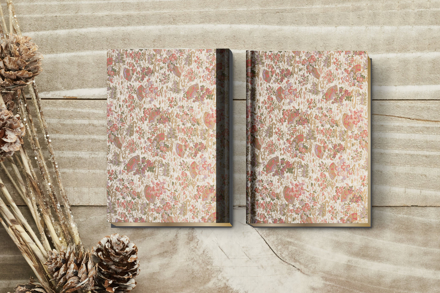 Two notebooks with floral and leaf patterned with red, green, and brown colors wrapped with chiyogami paper on a wooden surface with pine cones.