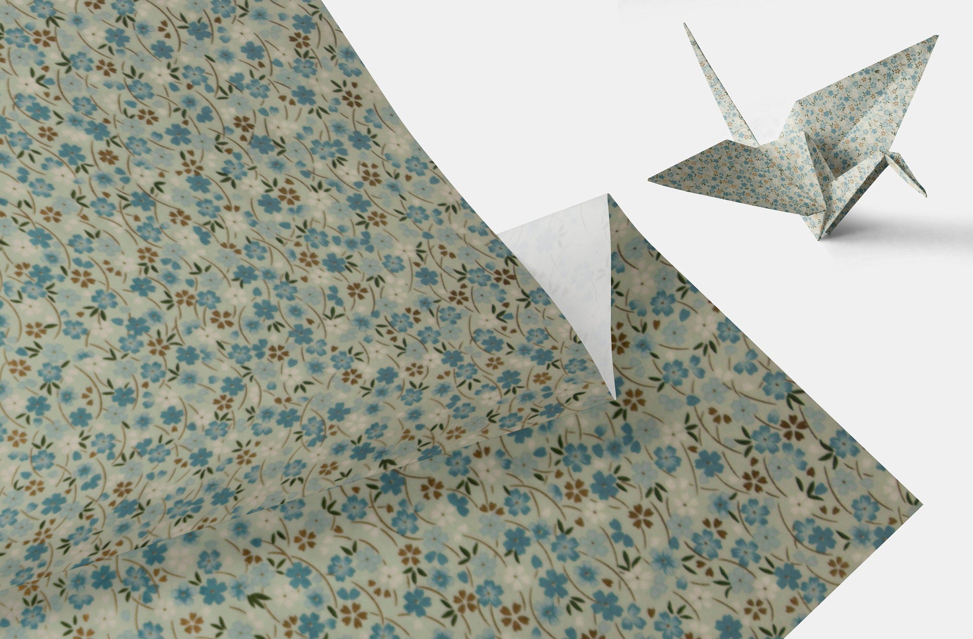 Floral-patterned chiyogami paper with a folded corner and an origami crane on a white background