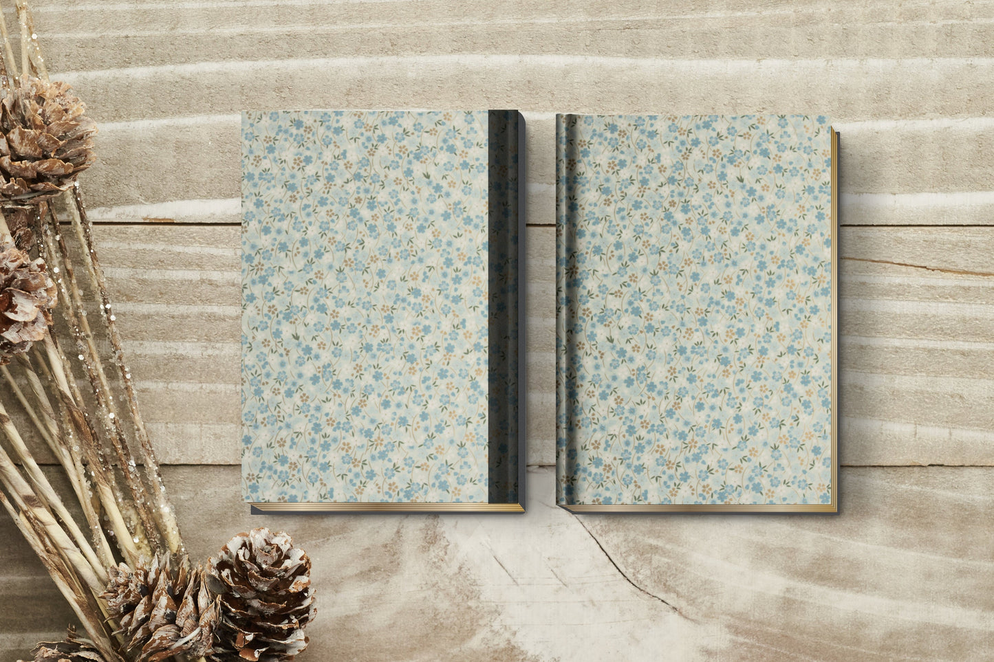 two notebooks with floral pattern made with chiyogami paper in a bookbinding project on a wooden surface with pine cones and branches.