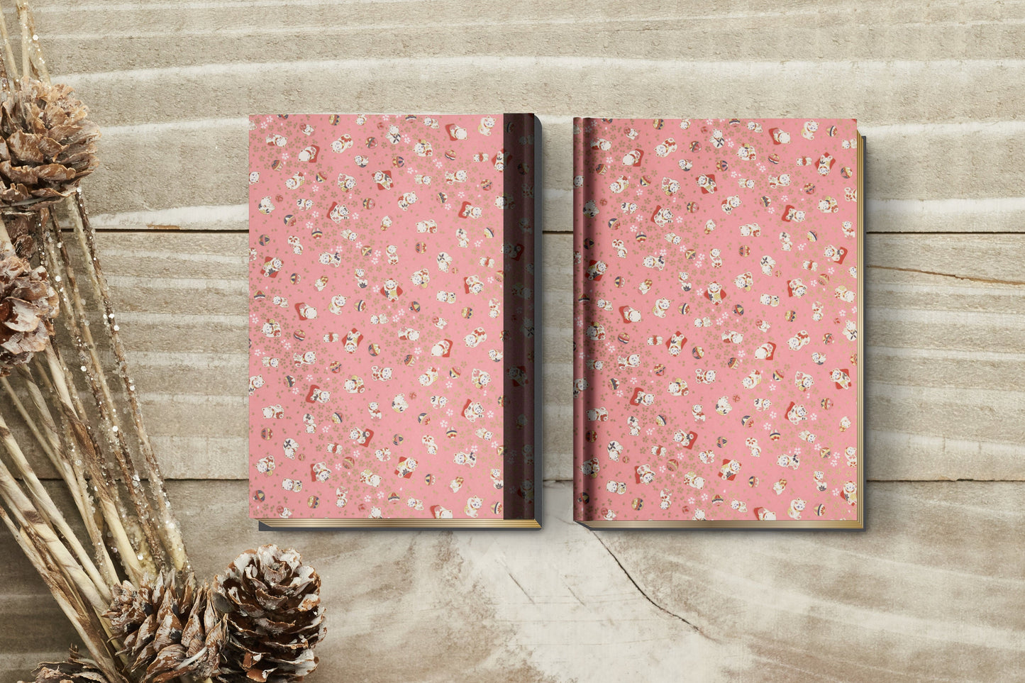 Two pink patterned books on a wooden surface with dried plants.