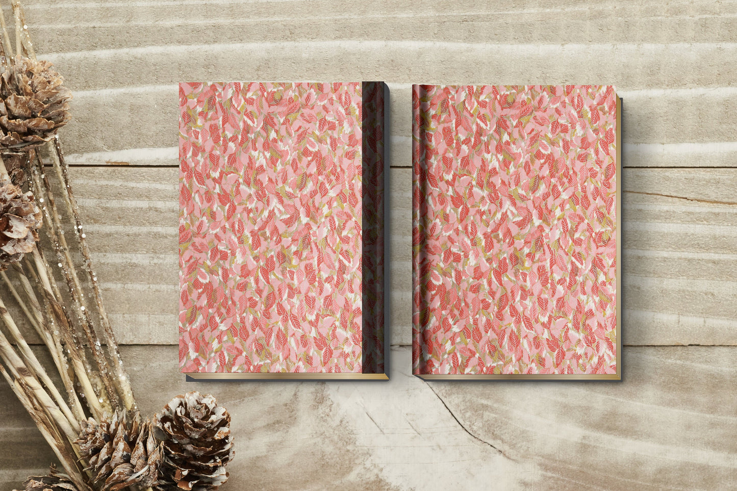 Two pink patterned books made with chiyogami paper in a bookbinding project on a wooden surface with decorative elements.