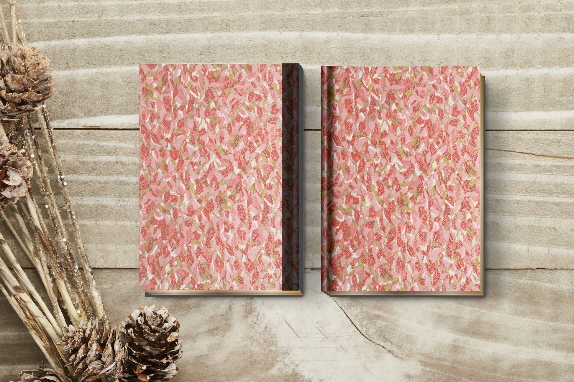 Two pink patterned books made with chiyogami paper in a bookbinding project on a wooden surface with decorative elements.