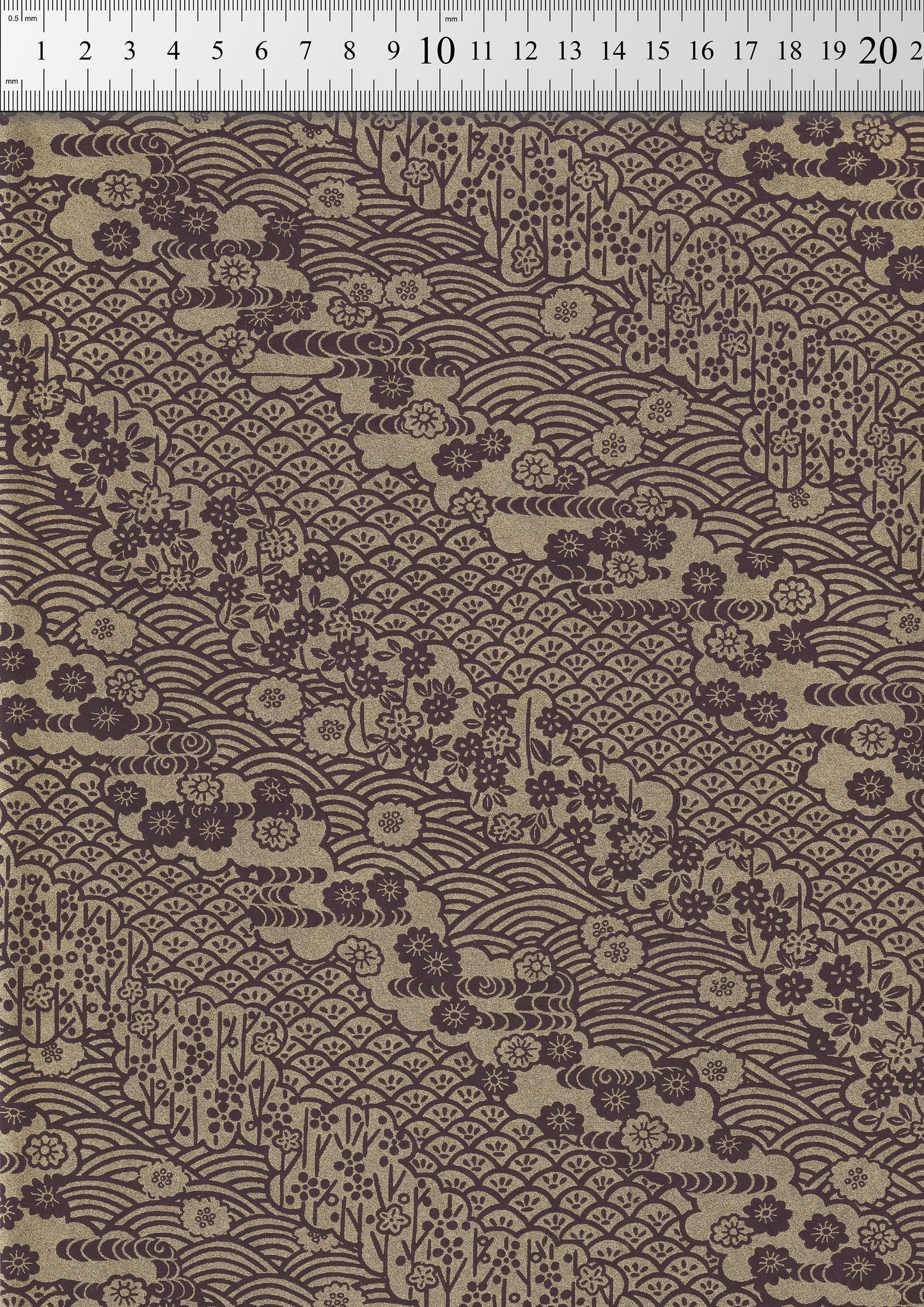 Textile with floral and wave pattern on a brown background, measured against a ruler.