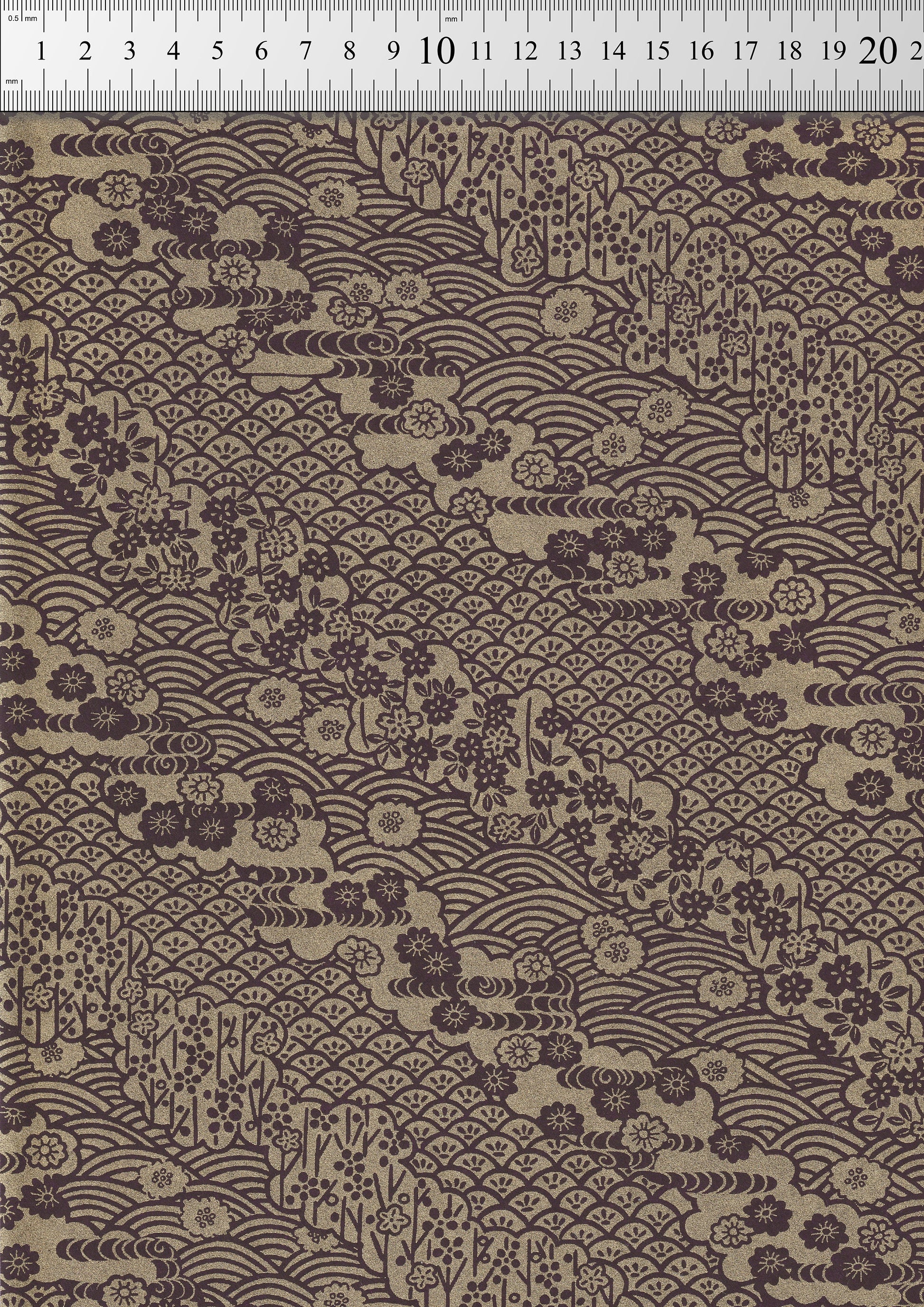 Textile with floral and wave pattern on a brown background, measured against a ruler.