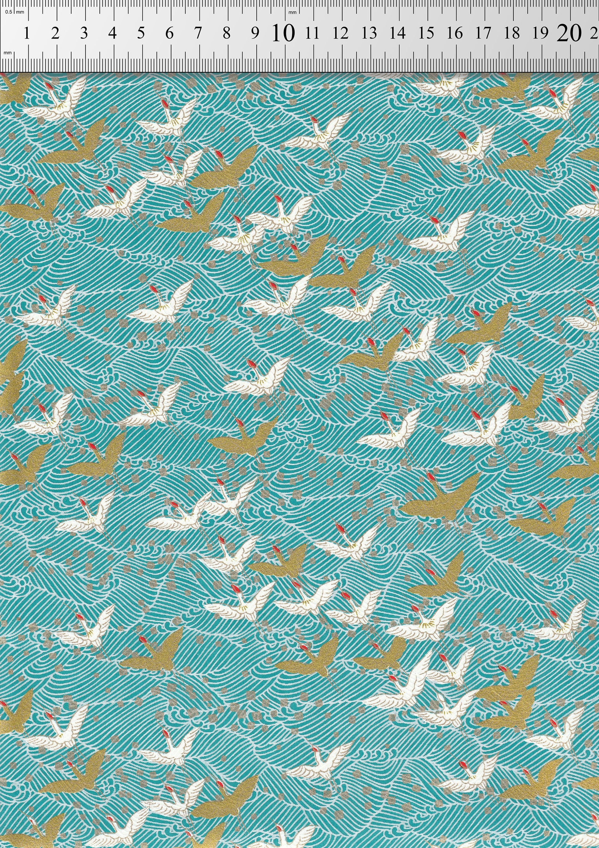 Chiyogami paper with Pattern of white and gold cranes on a teal background with a ruler for scale