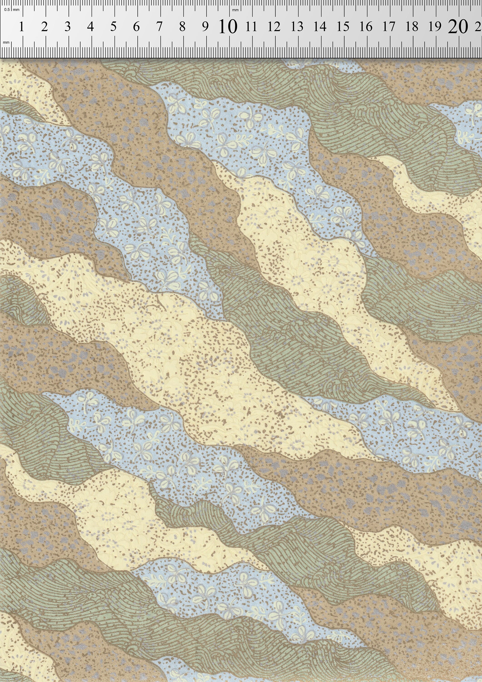 Textured chiyogami paper with wavy pattern in beige, brown, and blue on a white background with a ruler for scale