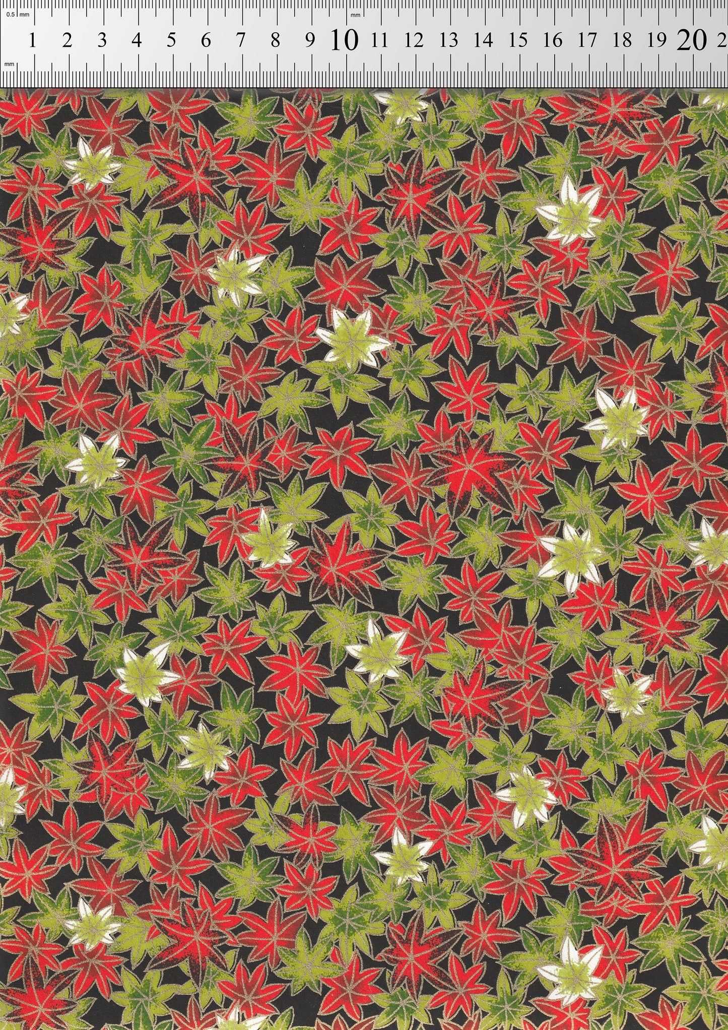 Patterned  chiyogami paper with red, green, and white flowers on a black background, measured against a ruler.