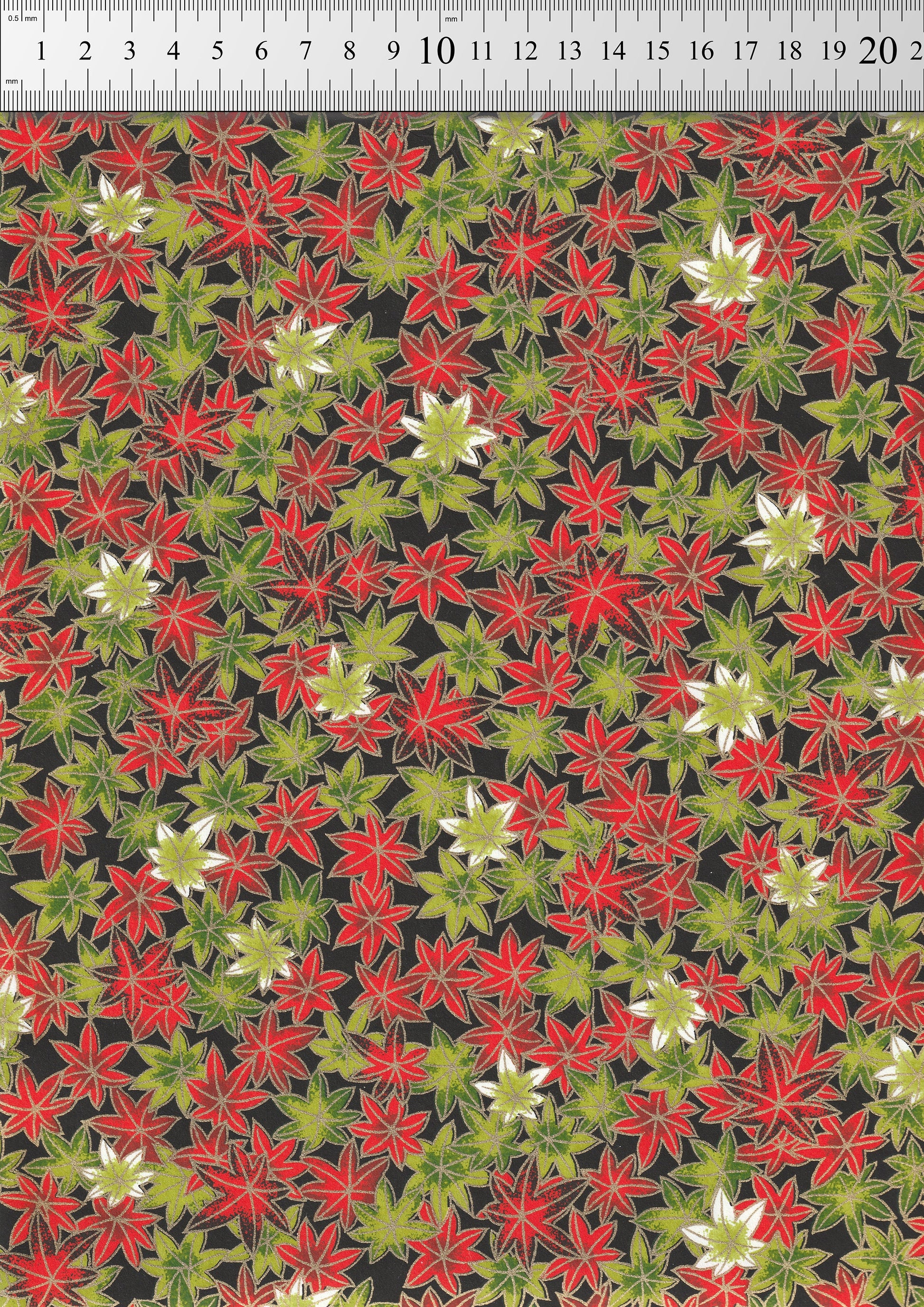 Patterned  chiyogami paper with red, green, and white flowers on a black background, measured against a ruler.